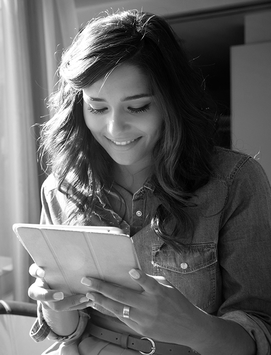 Young girl sitting by a window looking at a tablet and smiling..