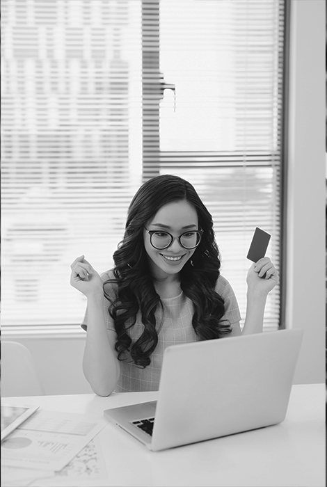 Girl with glasses holding credit/debit card online shopping at home with laptop.