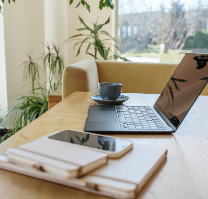 desk with notebook, devices, and plants in background