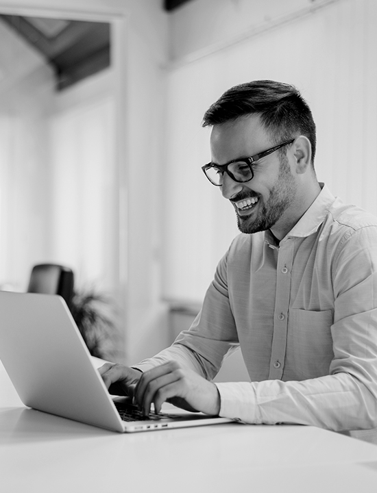 Man with glasses on his laptop working and smiling.