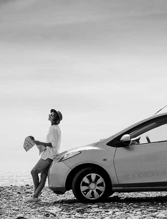 Girl with hat holding a map leaning against her car.